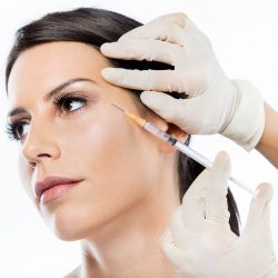 Portrait of beautiful young woman getting botox cosmetic injection in her face over white background.